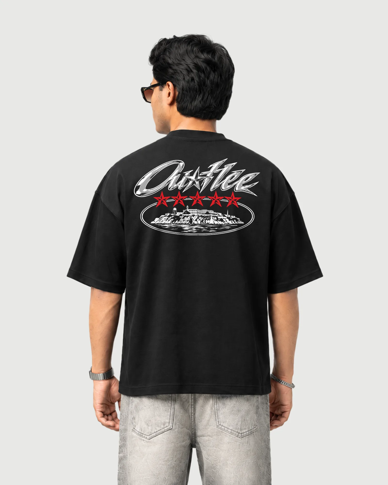 Model wearing the black Outflee Five Star Escape drop shoulder T-shirt, back view showing chrome Outflee lettering, five red stars and island artwork.