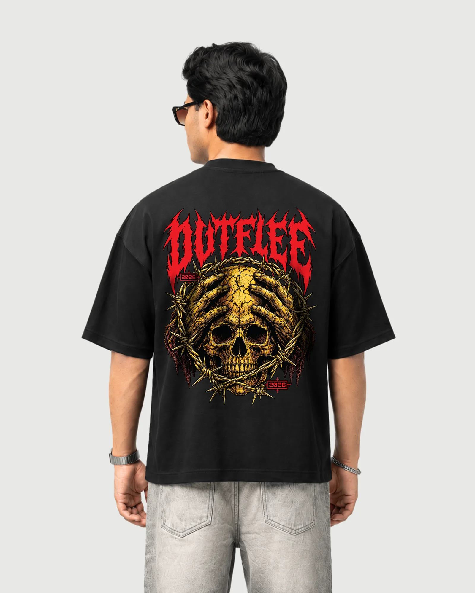 Model wearing the black Outflee Thornbound Skull T-shirt, back view showing a gold skull, skeletal hands, thorns and red lettering.