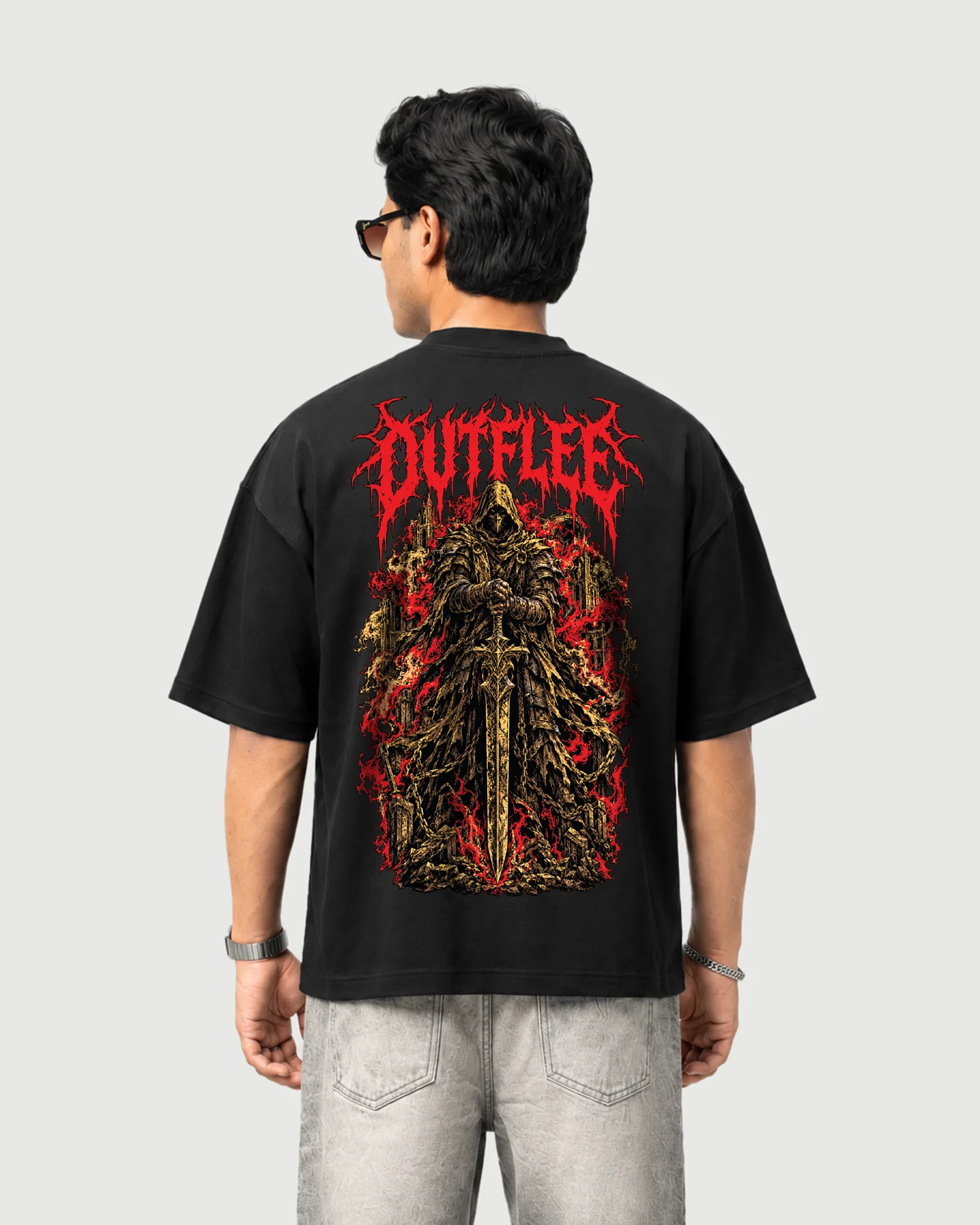 Model wearing the black Outflee Crimson Warden drop shoulder T-shirt, back view showing the large armored hooded warrior, sword, gothic ruins and red artwork.