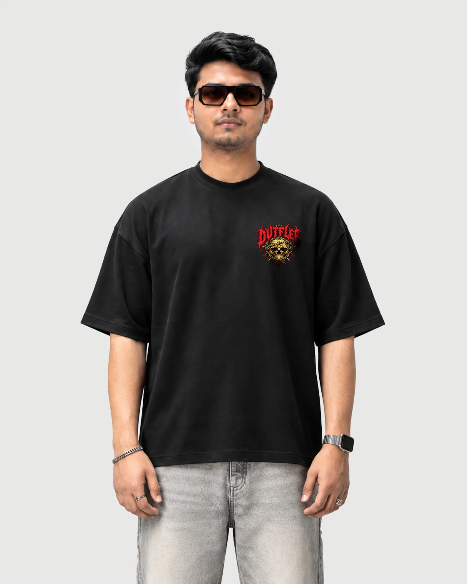 Model wearing the black Outflee Thornbound Skull drop shoulder T-shirt, front view with a small red and gold skull chest graphic.