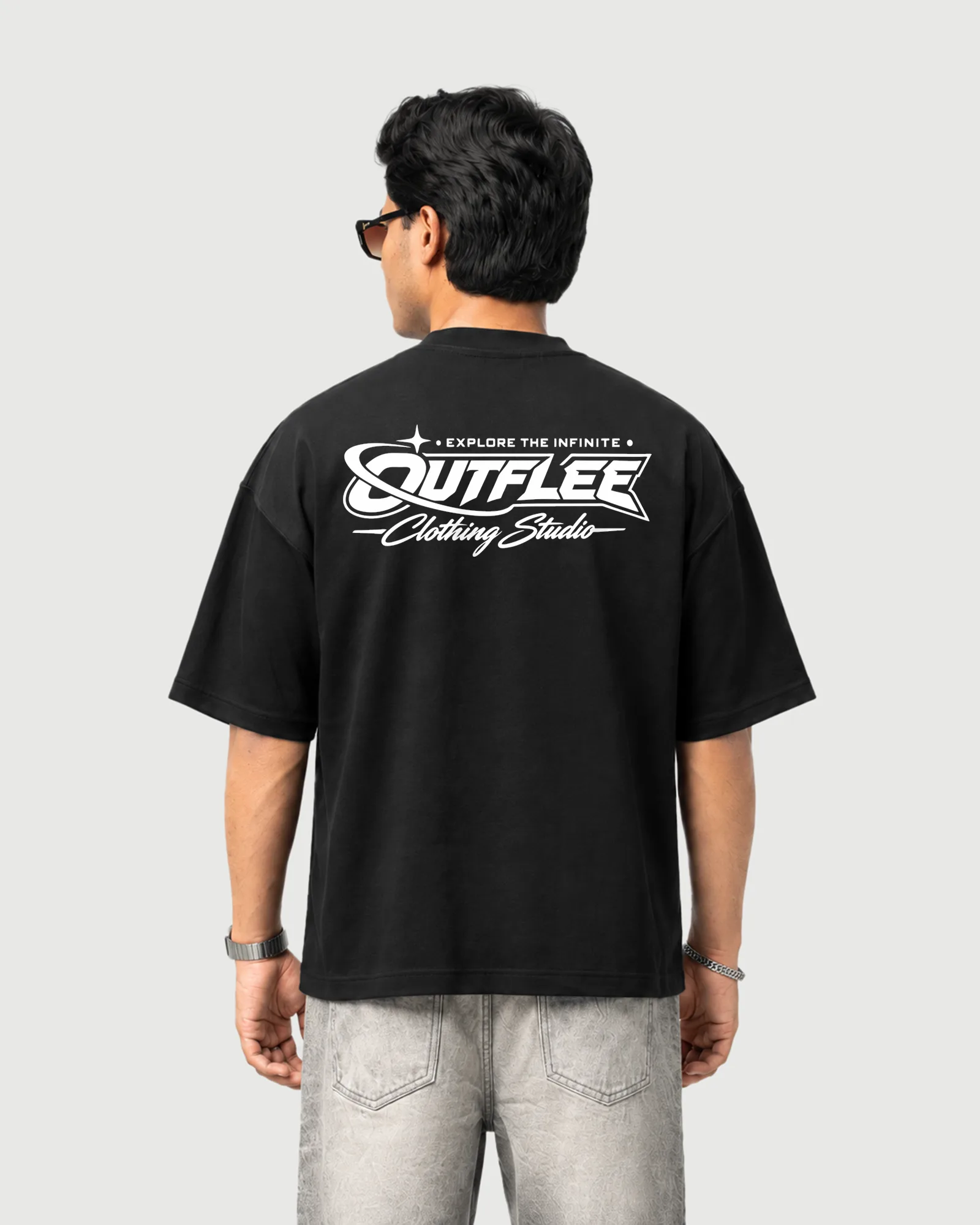 Model wearing the black Outflee Infinite Orbit drop shoulder T-shirt, back view showing bold Outflee typography, orbit graphics and Explore the Infinite artwork.