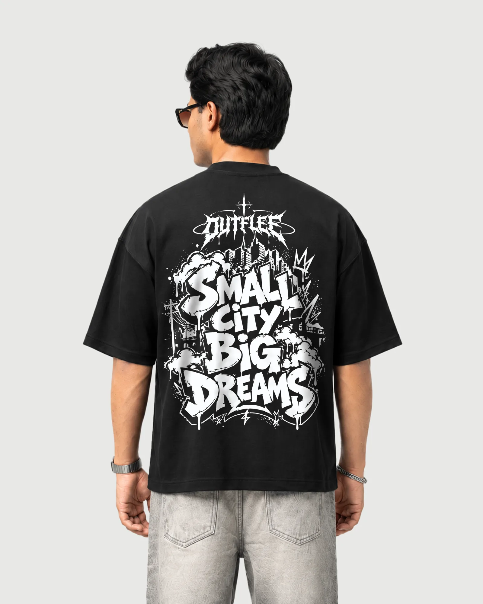 Model wearing the black Outflee Small City Big Dreams T-shirt, back view showing the large white graffiti-style Small City Big Dreams artwork.