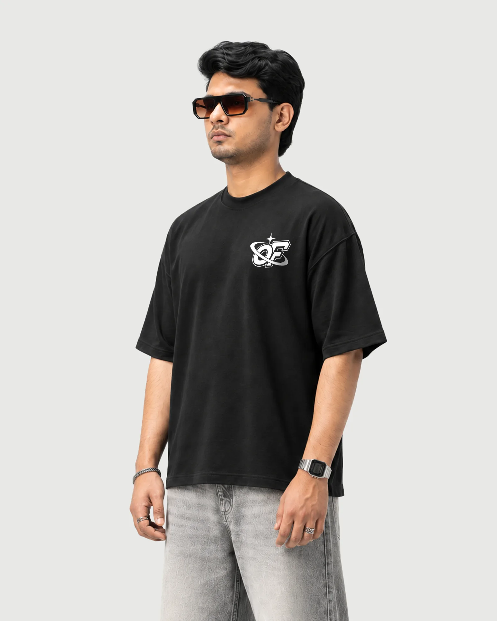 Three-quarter view of a model wearing the black Outflee Infinite Orbit drop shoulder T-shirt, showing the relaxed fit and orbit-inspired chest graphic.