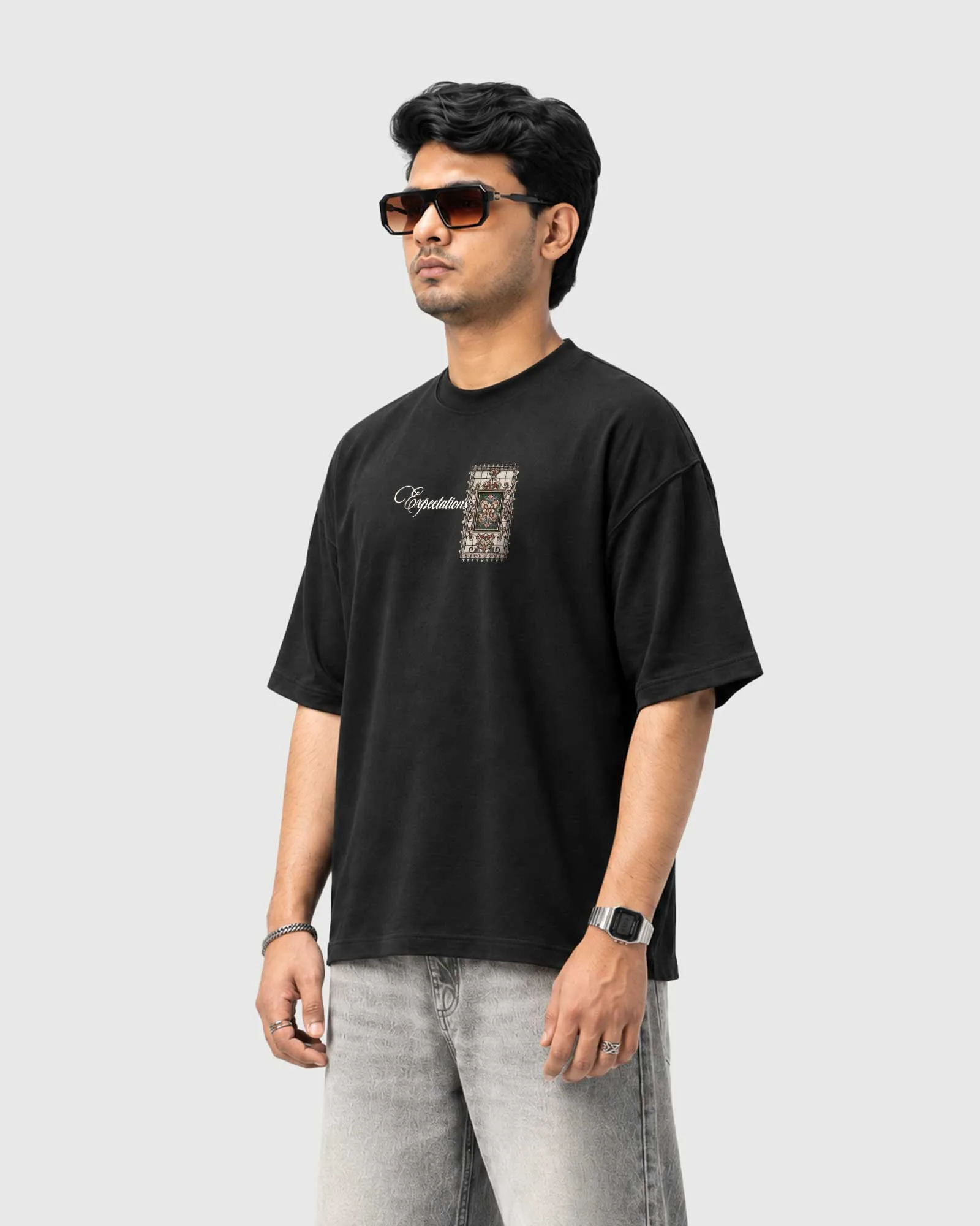 Three-quarter view of a model wearing the black Outflee Framed Expectations drop shoulder T-shirt, showing the relaxed fit and vintage-inspired front graphic.
