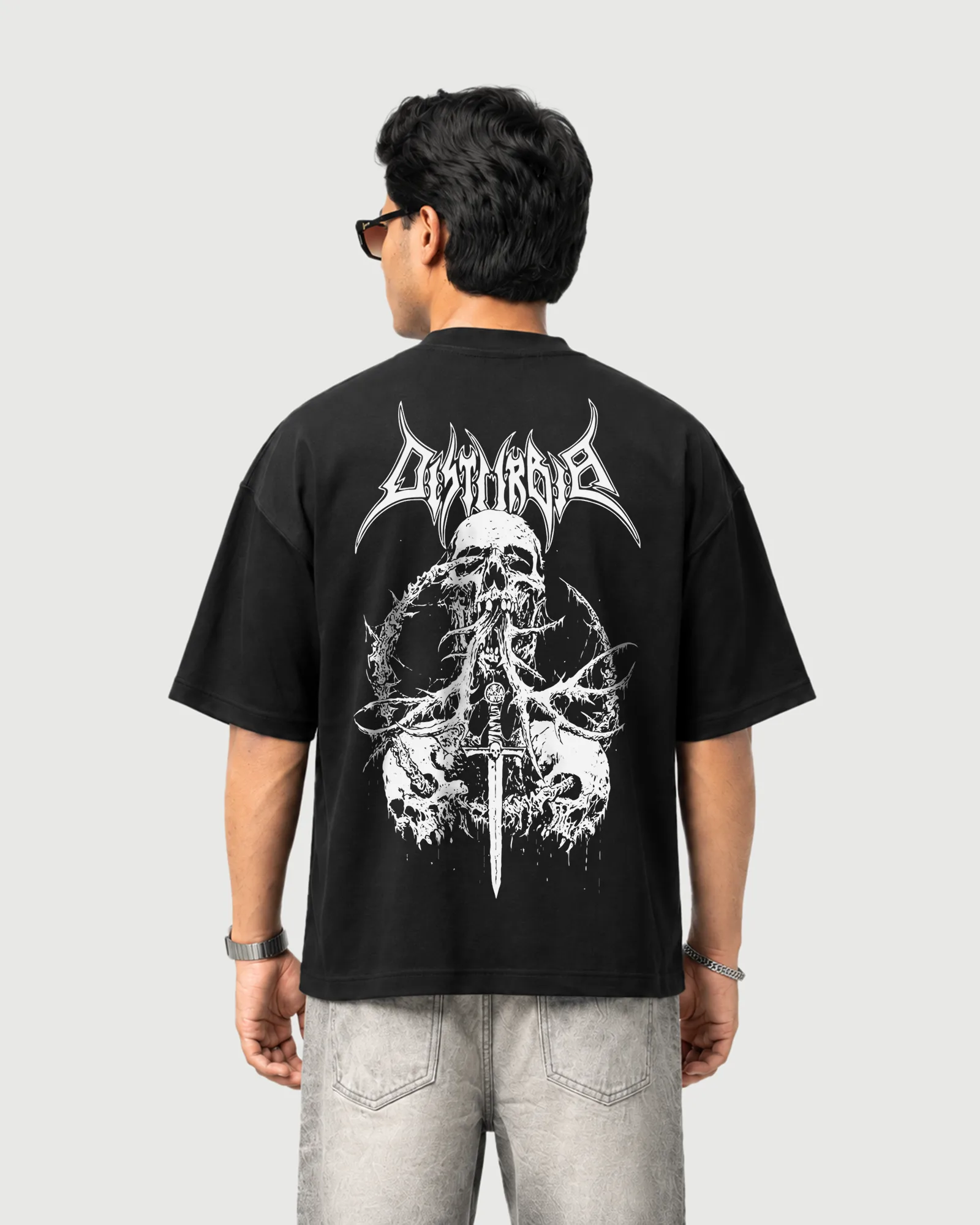 Model wearing the black Outflee Skullbound drop shoulder T-shirt, back view showing the large skull, thorn and dagger artwork with gothic Outflee lettering.