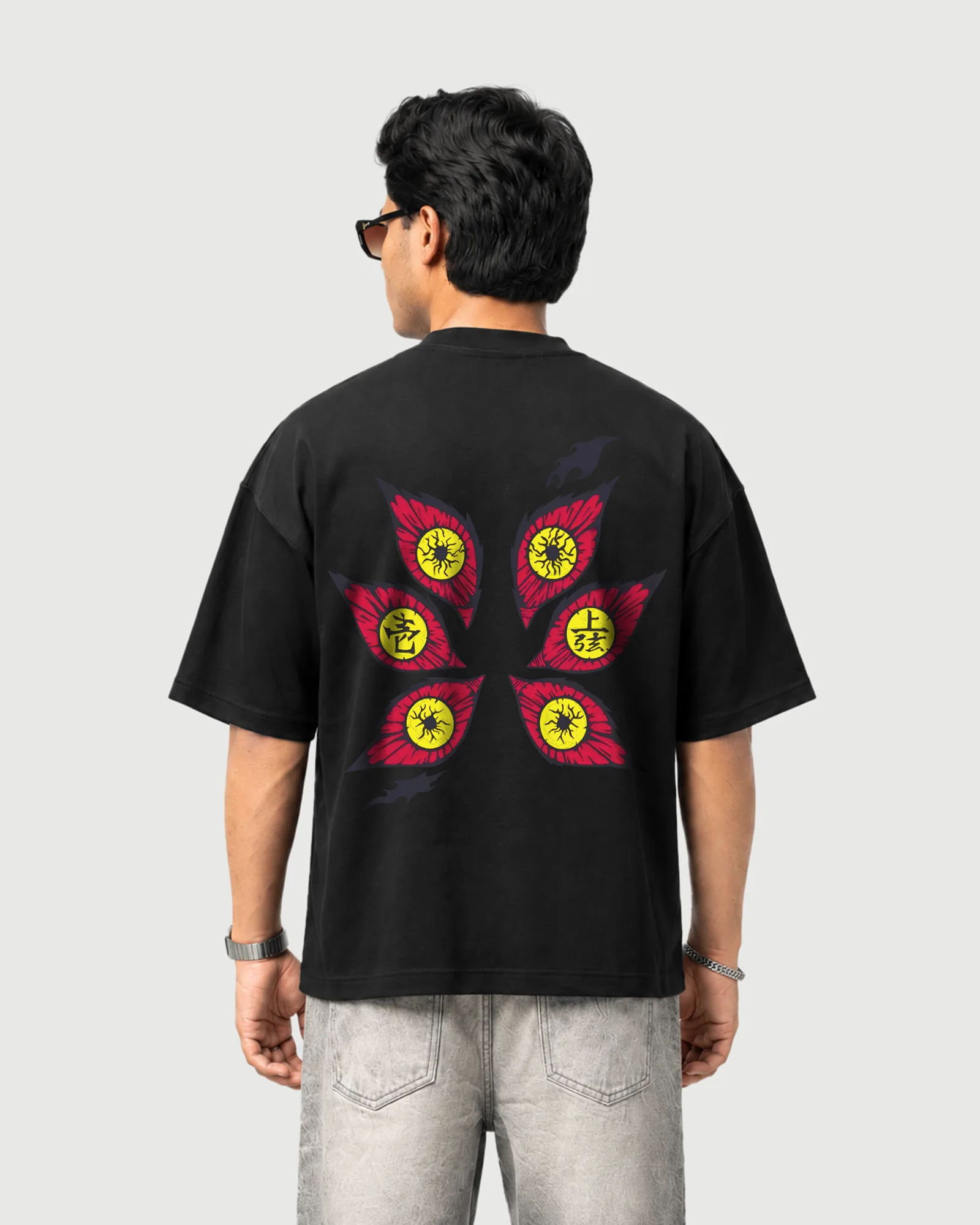 Model wearing the black Outflee Sixfold Gaze drop shoulder T-shirt, back view showing the large six-eye red and yellow graphic composition.