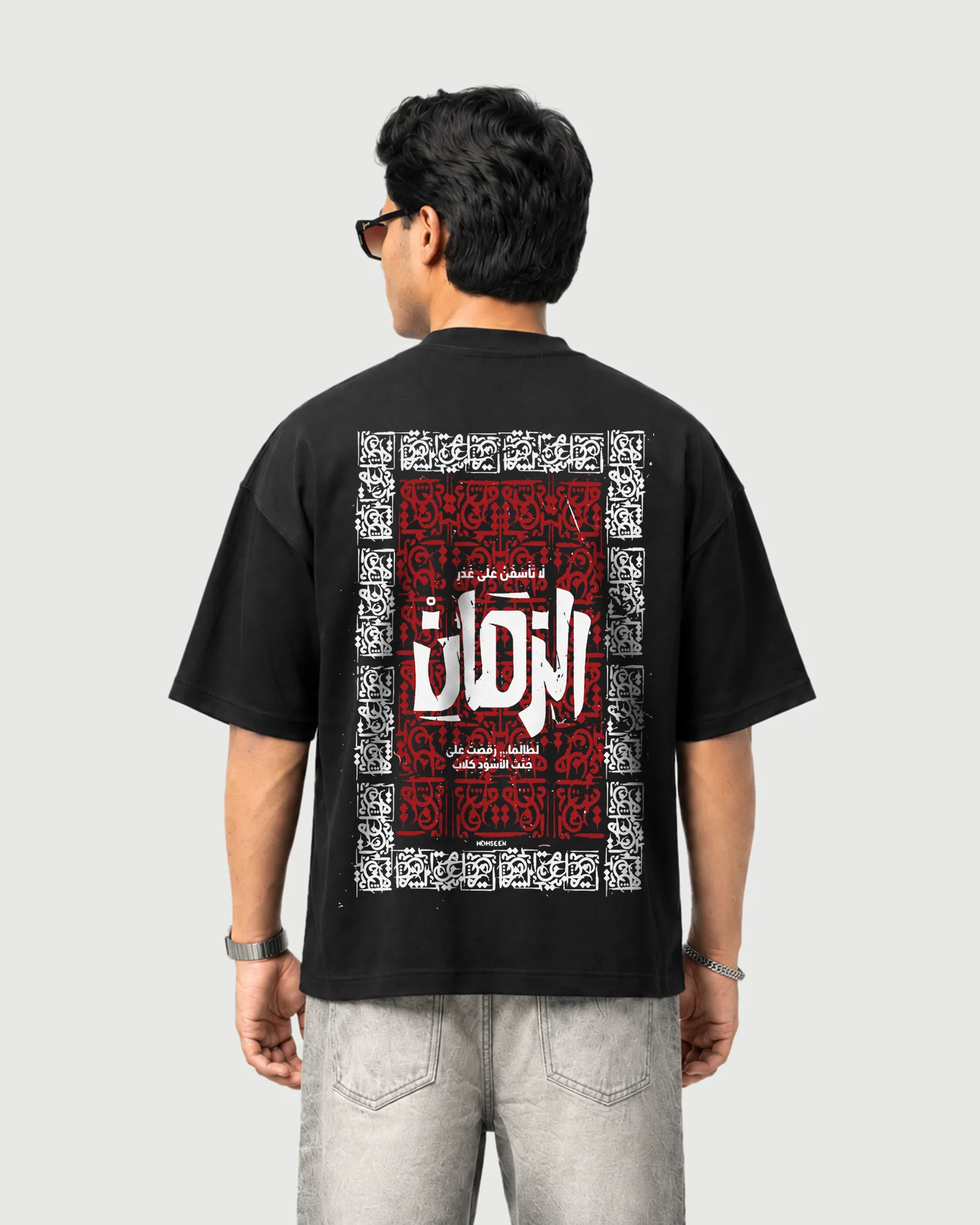 Model wearing the black Outflee Arabic Calligraphy drop shoulder T-shirt, back view showing the large red and white framed Arabic calligraphy artwork.